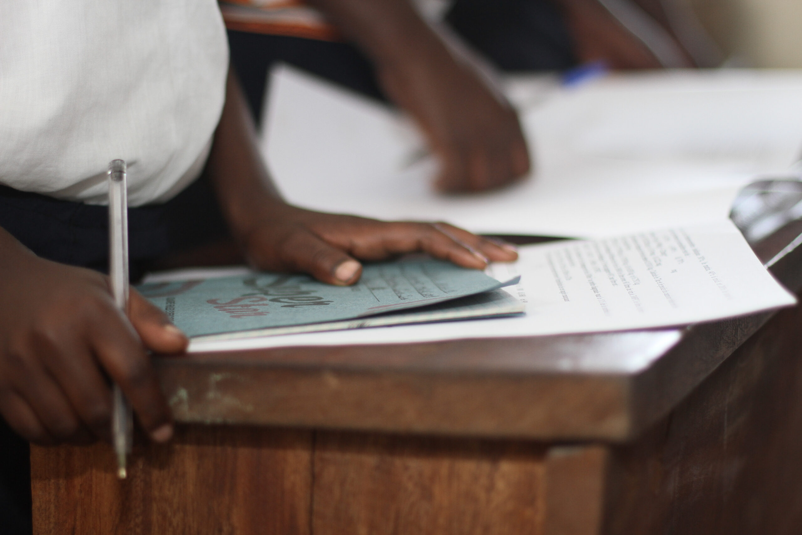 A book on a wooden desk. The child is holding a pen over the book